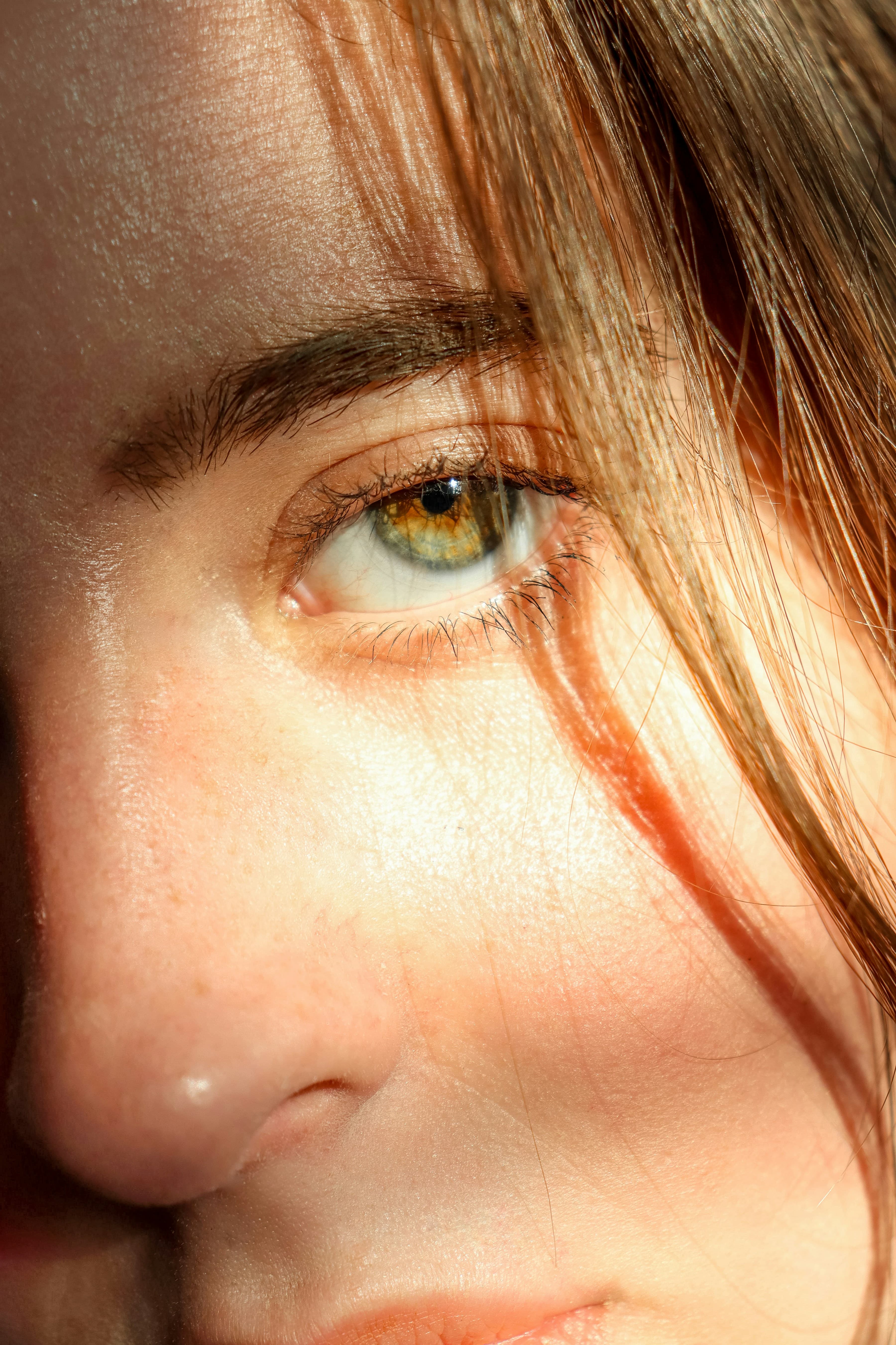 Sunlit close-up of natural skin and hair framing a hazel eye