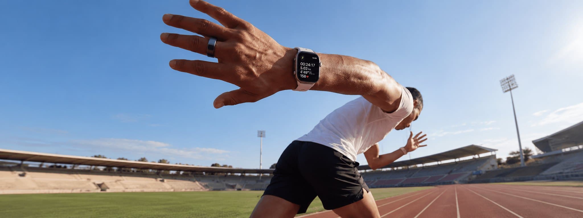 A sprinter driving out of the blocks on an outdoor track, wearing a smartwatch and a smart ring